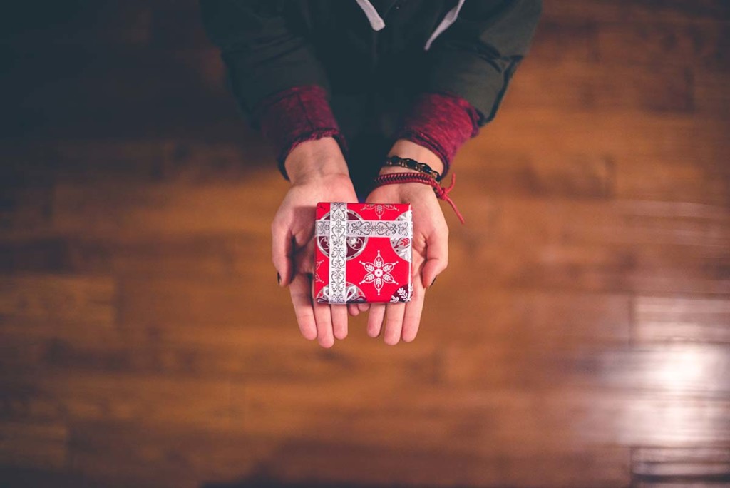 A person holding a small box wrapped in red holiday wrapping paper.